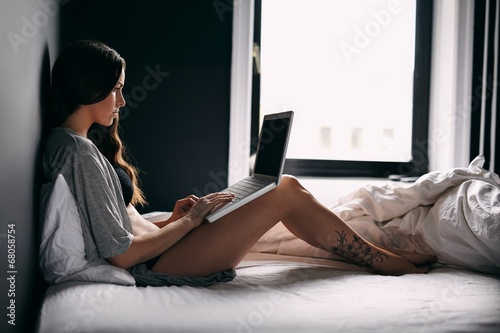 Young woman using laptop computer in bedroom photo