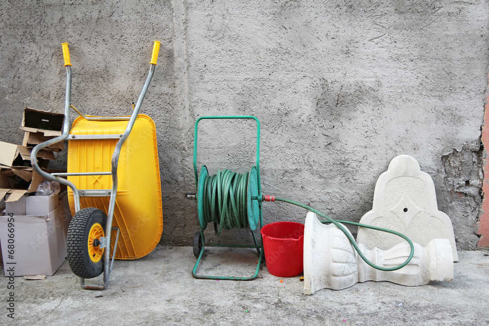 Wheelbarrow, hose and cartons in front of the concrete wall Wheelbarrow, hose and cartons in front of the concrete wall