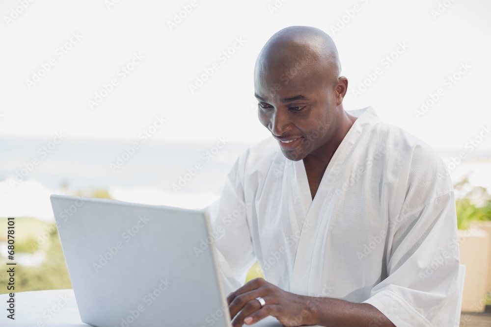 Handsome man in bathrobe using laptop at breakfast outside