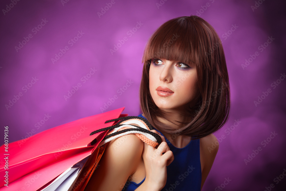 Brunette girl with shopping bags on violet background.