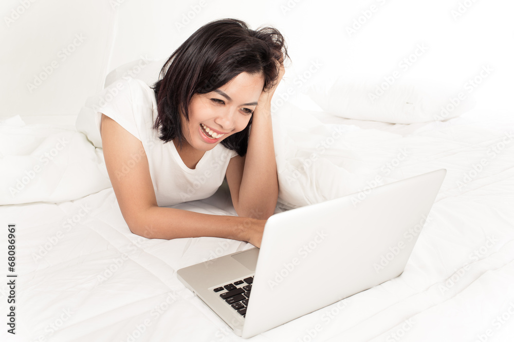 Smiling woman using a laptop while lying on her bed Smiling woman using a laptop while lying on her bed