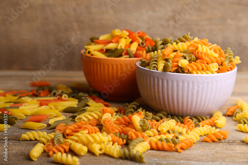 Assortment of colorful pasta in color bowls on wooden