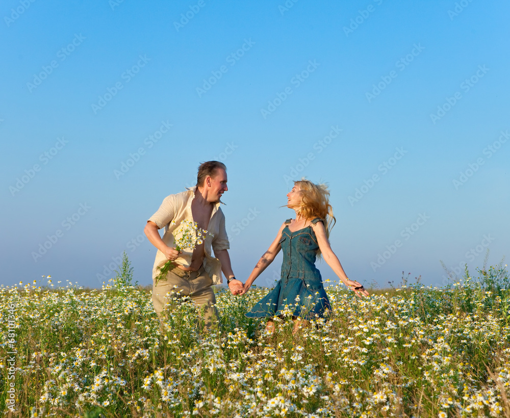 Fototapeta premium The happy young pair in the field of chamomiles