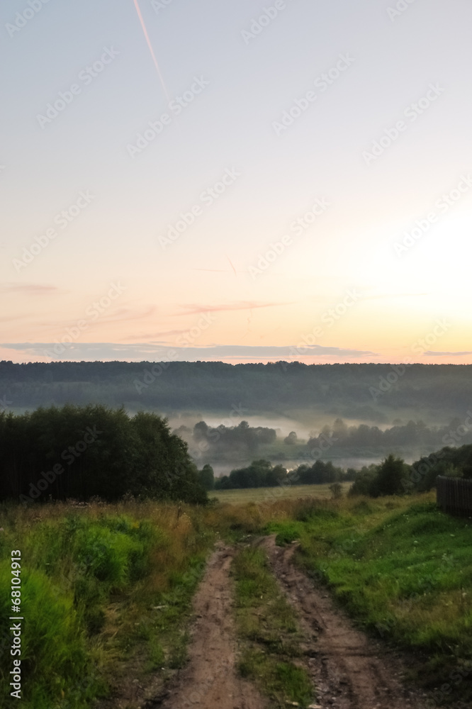 Obraz premium country road and fog over river in summer twilight