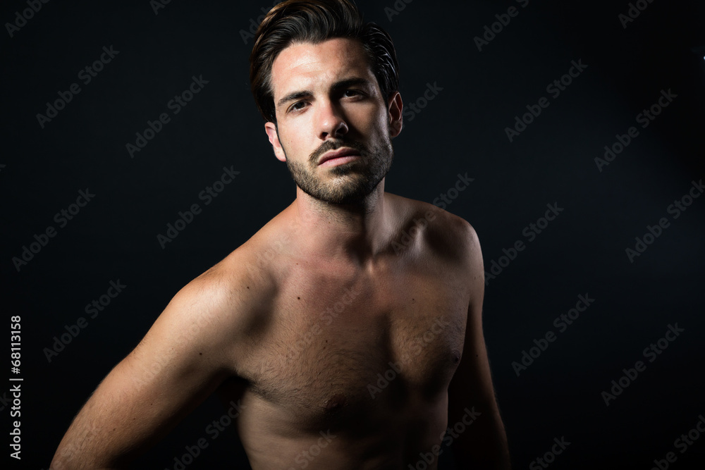 Handsome muscular male model posing over black background.