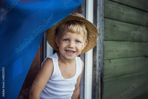 Cheerful kid with straw hat leaning out a window