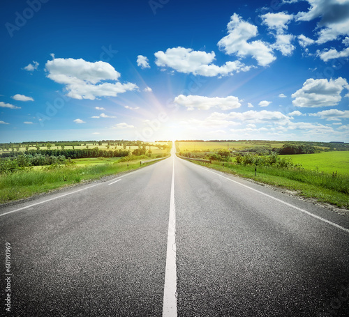 Asphalt road in field under blue sky