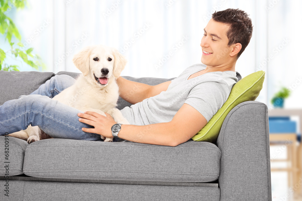 Young man sitting with his puppy on a sofa at home Young man sitting with his puppy on a sofa at home