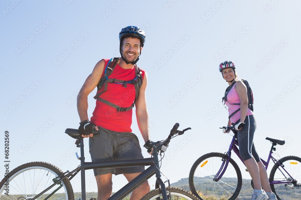 Fototapeta premium Fit cyclist couple standing at the summit smiling at camera