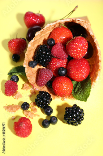 Different ripe berries in sugar cone, on yellow background