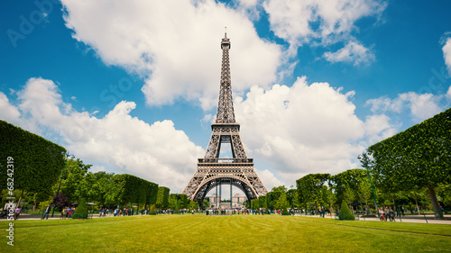 Eiffel Tower and gardens with people walking against blue cloudy