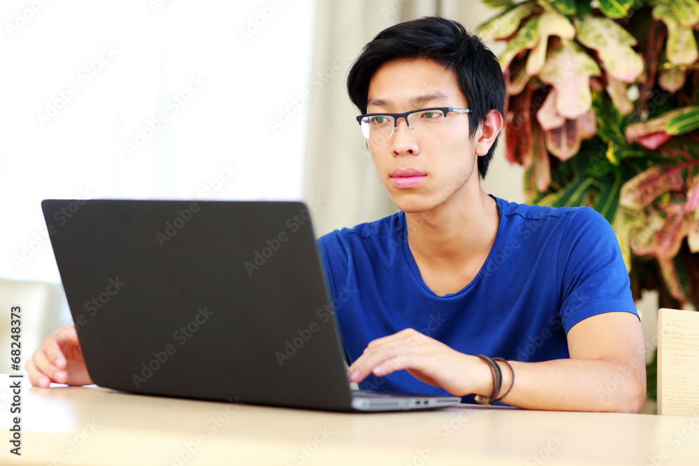 Serious asian man sitting at the table with laptop Serious asian man sitting at the table with laptop