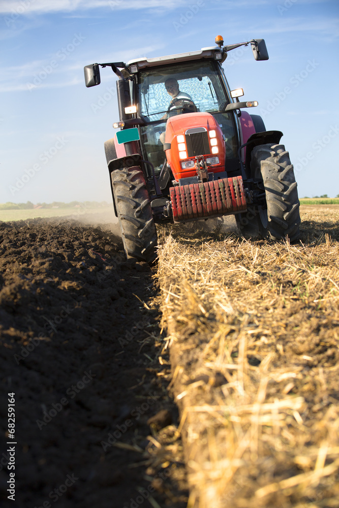 Naklejka premium Farmer plowing stubble field with red tractor