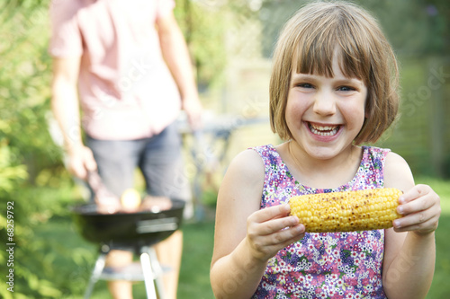 Young Girl Eating Sweetcorn At Family Barbeque photo