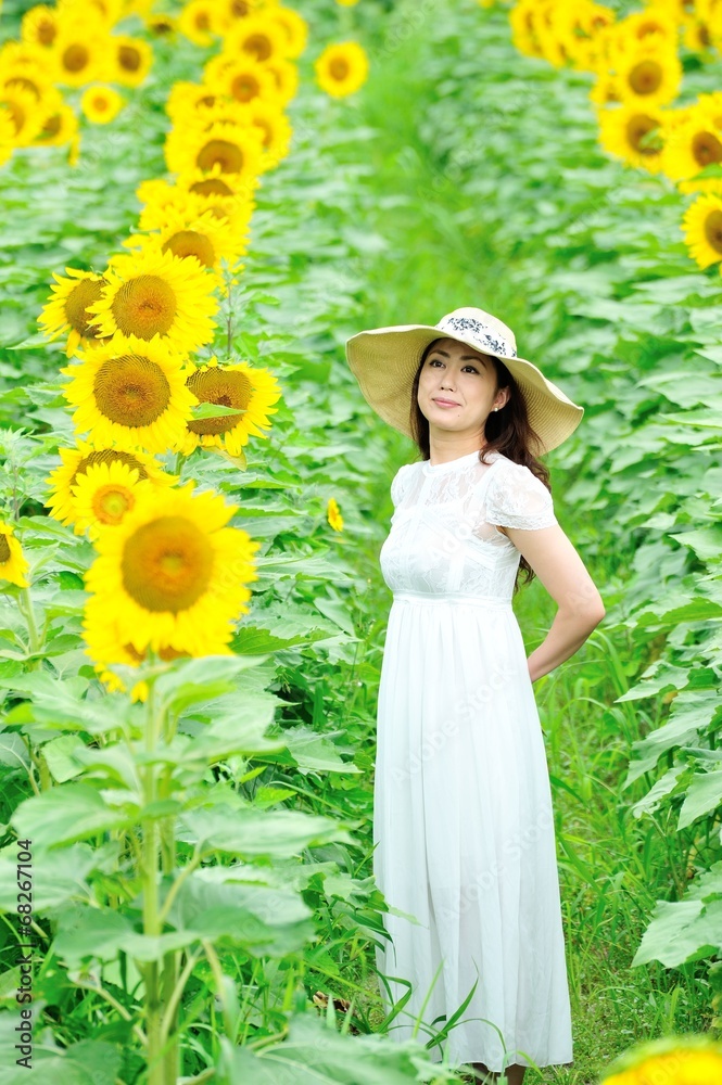 Photo Stock ひまわり畑に立っている白いワンピースと麦わら帽子を着ているアジア人の美しい女性 Adobe Stock