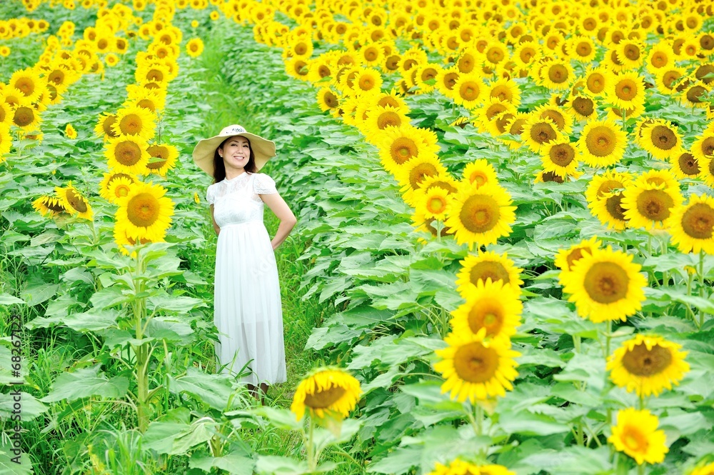 Photo Stock ひまわり畑に立っている白いワンピースと麦わら帽子を着ているアジア人の美しい女性 Adobe Stock