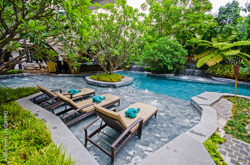 Poolside relax chairs in garden style swimming pool