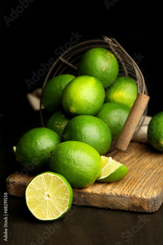 Fotografia Fresh juicy limes in basket on wooden table, on dark background