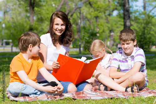 teacher reads a book to children in a summer park