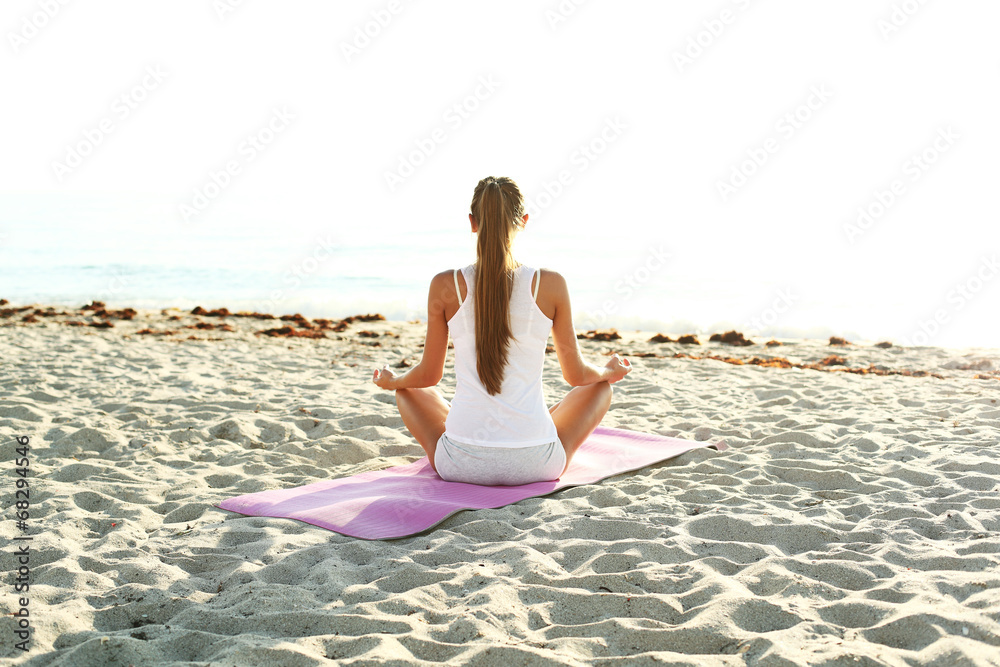 young woman doing yoga on the beach at sunrise.