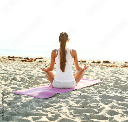 young woman doing yoga on the beach at sunrise.