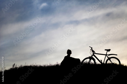 Silhouette of tourist and bike on sky background