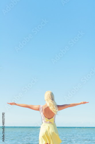 Young woman with arms wide open near the sea. Place for text.