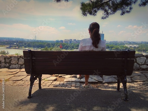 Girla sitting on a bench, watching city panorama photo