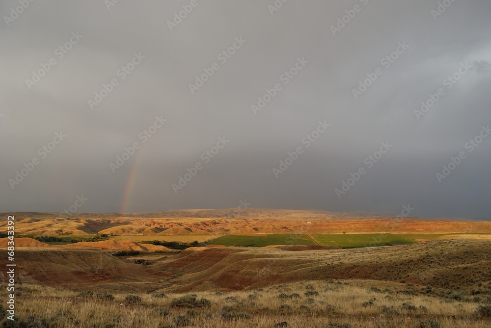 landscape of mountains and fields with heavy clouds and rainbow