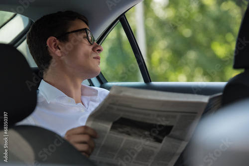 Businessman reading newspaper car