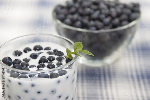 Blueberries with yogurt in a glass and blueberries in a vase.
