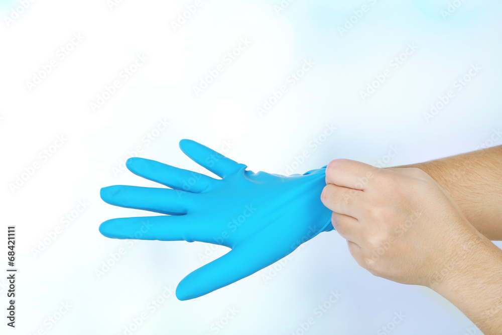 Doctor putting on protective gloves, on light background