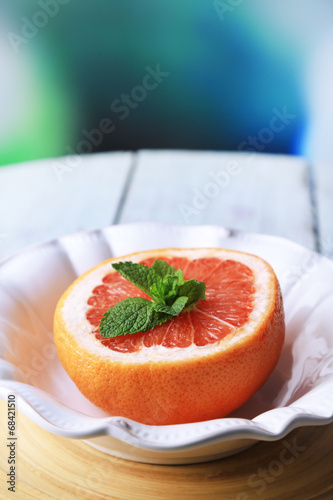 Ripe grapefruits on plate on color wooden background