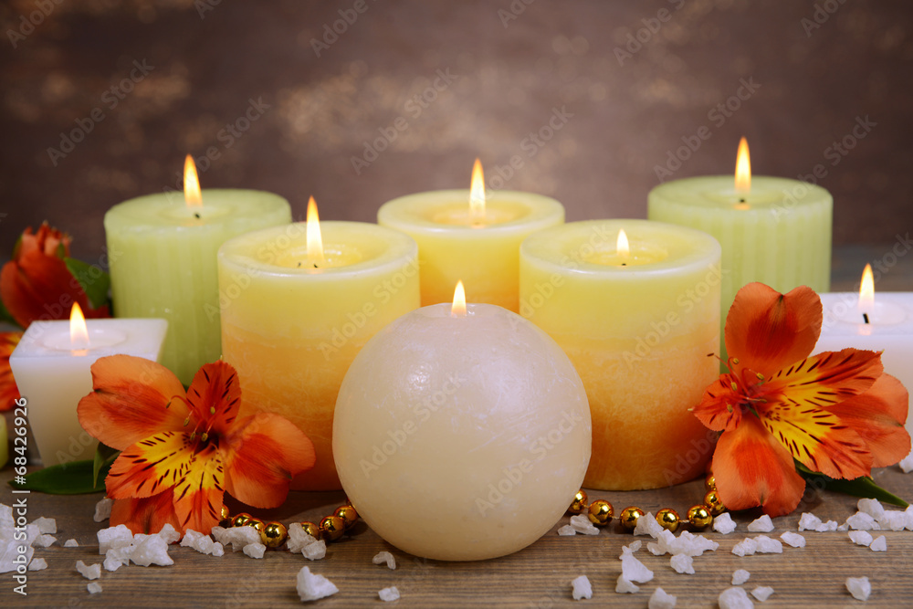 Beautiful candles with flowers on table on brown background Beautiful candles with flowers on table on brown background