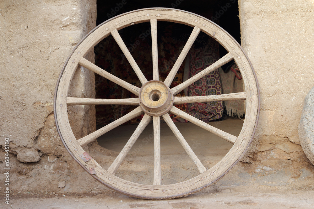 An old wooden wagon wheel leaning up against soil wall An old wooden wagon wheel leaning up against soil wall