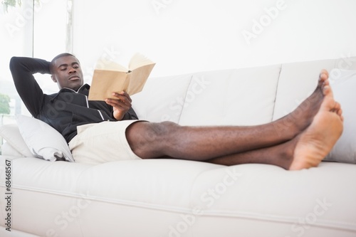 Casual man sitting on his sofa reading a book