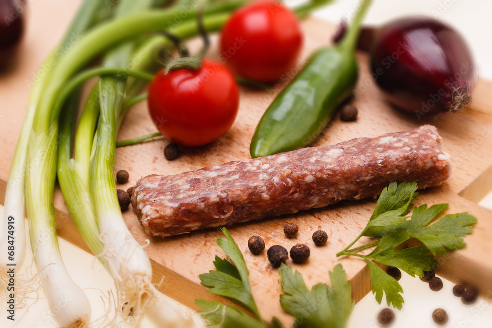 raw kebapcheta with vegetables on wooden board