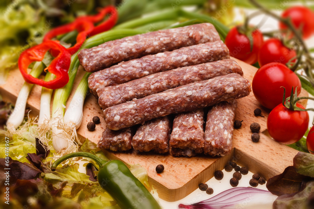 raw kebapcheta with vegetables on wooden board raw kebapcheta with vegetables on wooden board
