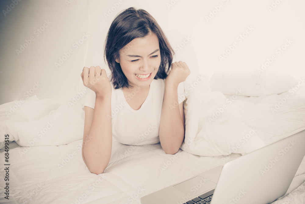 Smiling woman using a laptop while lying on her bed Smiling woman using a laptop while lying on her bed