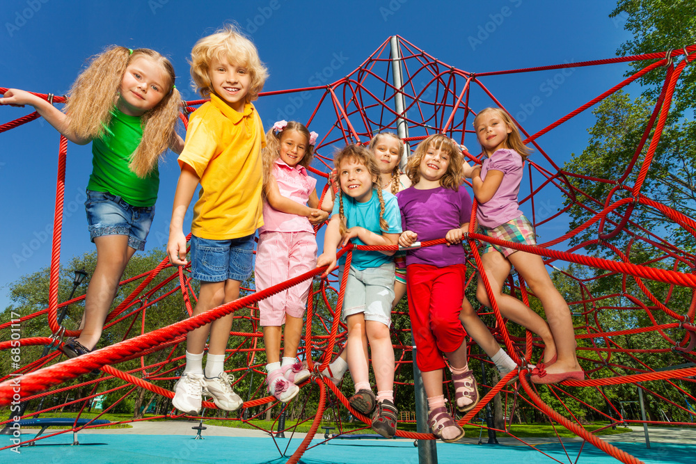 Happy kids stand on red ropes of playground