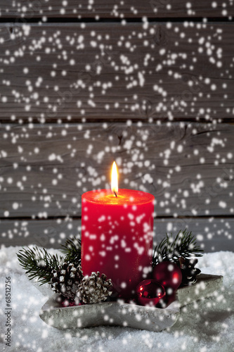 Adventsgesteck mit roter Kerze auf Schnee vor Holzhintergrund