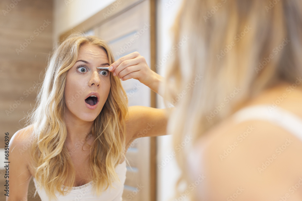 Fototapeta premium Scared woman tweezing eyebrows in bathroom