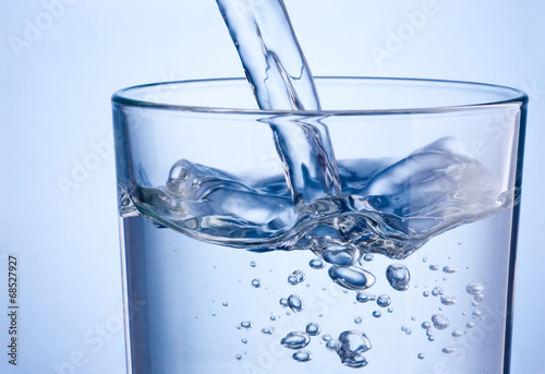 Close-up pouring water into glass on a blue background