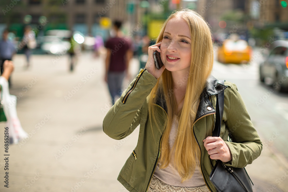 Young caucasian blond woman in city talking on cellphone