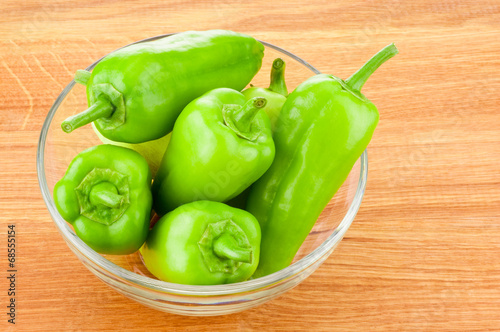 Green peppers in transparent glass bowl on wooden board