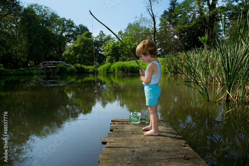 Little Boy Fishing from Wooden Dock on a Lake in Sunny Day