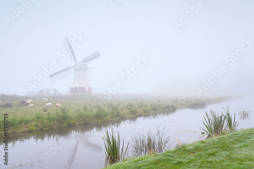 windmill and sheep by river in fog