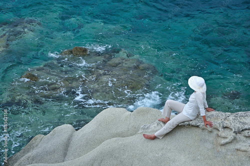Woman with a hat sitting on the rock near the sea