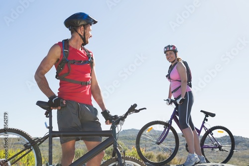 Fit cyclist couple standing at the summit smiling at each other