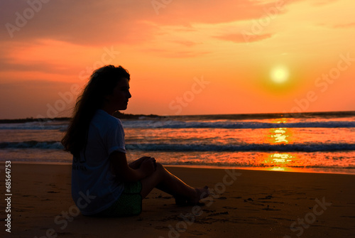 The silhouette ot girl sits on the beach. Enjoys a decline